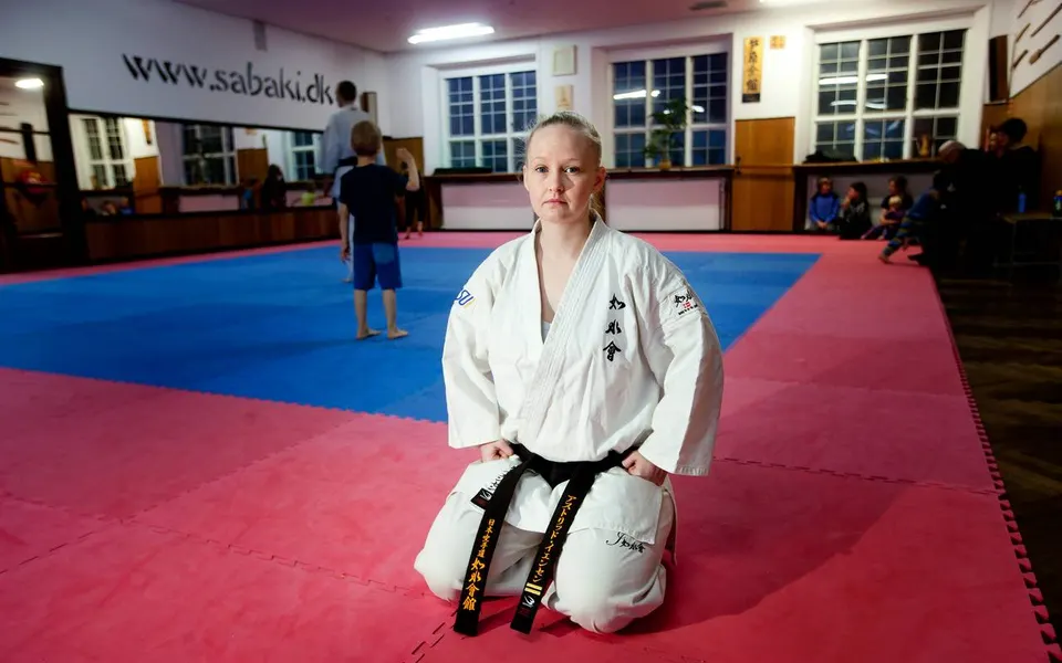 Astrid Jensen i hvid dragt og sort bælte, knælende på måtten i klubbens dojo
